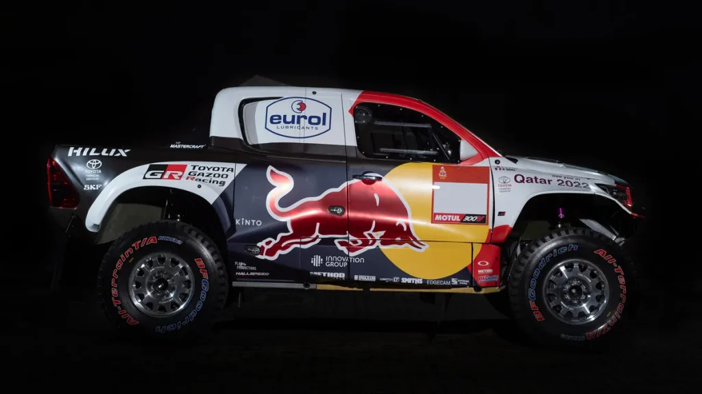 Toyota Hilux DKR GR FC vätgasdriven racerbil med Red Bull-logotyp, sponsorlogotyper och Qatar 2022-märkning på svart bakgrund.