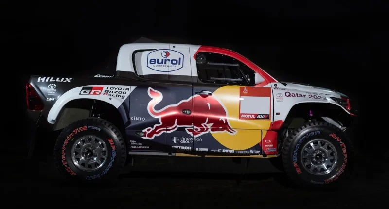 Toyota Hilux DKR GR FC vätgasdriven racerbil med Red Bull-logotyp, sponsorlogotyper och Qatar 2022-märkning på svart bakgrund.